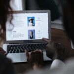 Two adults reviewing child adoption profiles on a laptop screen, considering potential matches.